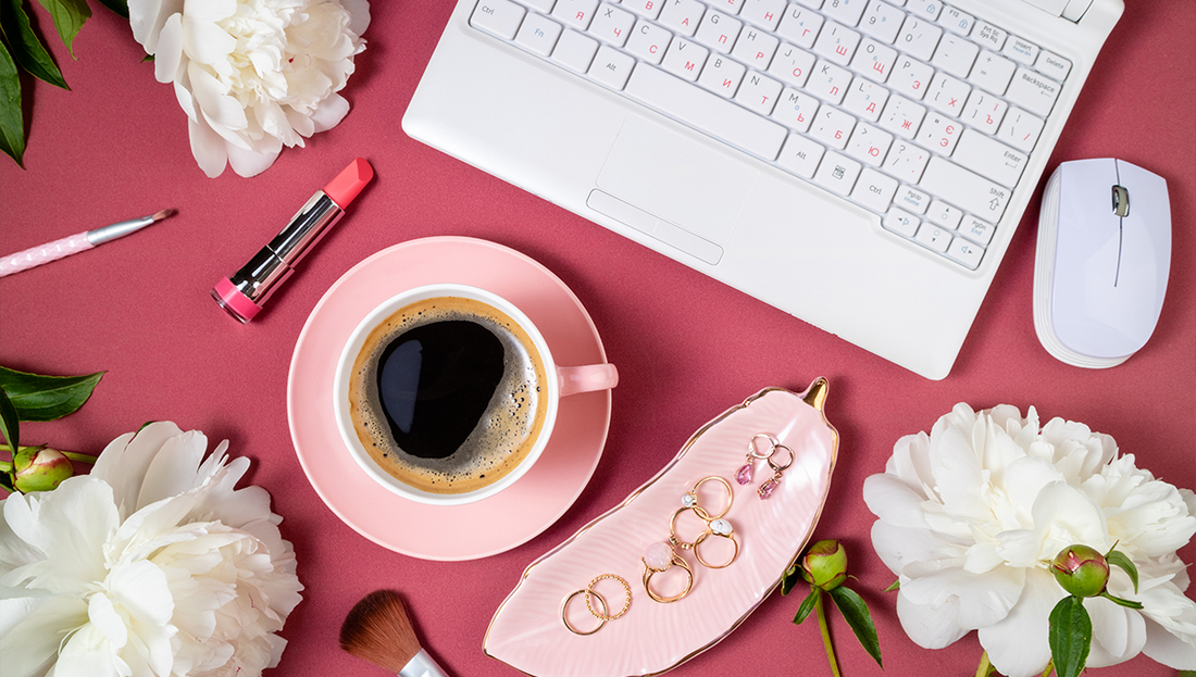 Flat lay with a cup of coffee, white flowers, lipstick, and jewelry on a pink background — symbolizing femininity, beauty, and self-care during Pink October.