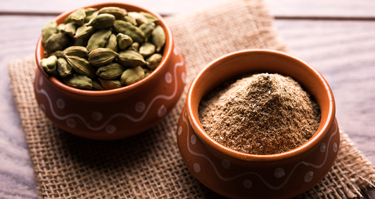 Whole and ground cardamom pods in clay bowls on a rustic burlap surface
