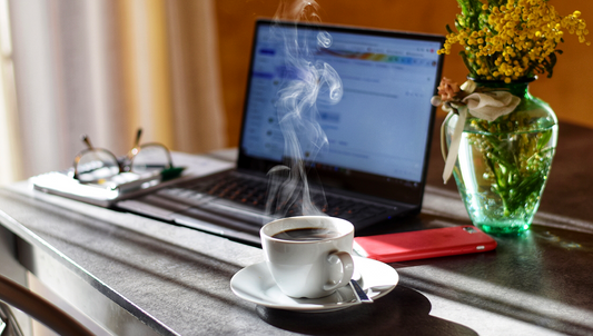 Steaming cup of coffee next to laptop and flowers on a desk — energizing the workday.