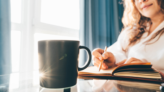 Woman holding a cup of coffee by a bright sunny window with books and flowers, embracing a calm morning ritual.
