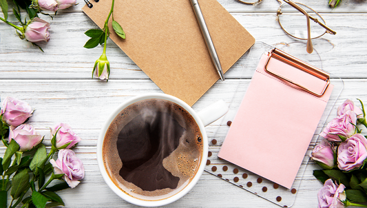 Cup of steaming black coffee on a desk with notebook, pen, and pink roses, symbolizing mindfulness, relaxation, and coffee rituals.