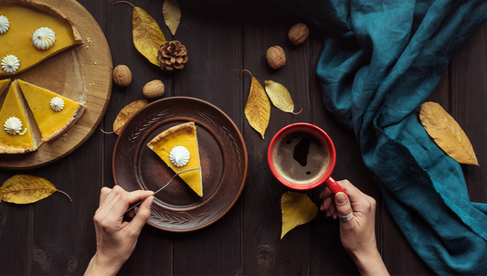 Slice of pumpkin pie with coffee on a rustic dark table surrounded by autumn leaves and warm fall colors — perfect Thanksgiving atmosphere.
