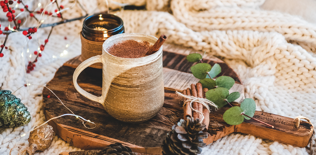 A ceramic mug filled with spiced coffee topped with cinnamon, surrounded by natural winter elements on a wooden board.