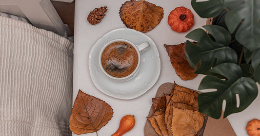Autumn-inspired coffee setup with a mug surrounded by dried leaves and mini pumpkins, symbolizing mindful fall mornings with Yasma Coffee.