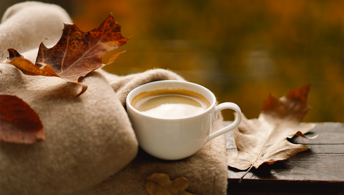 Cozy cup of coffee on a wool blanket with autumn leaves scattered around, evoking warm fall vibes.
